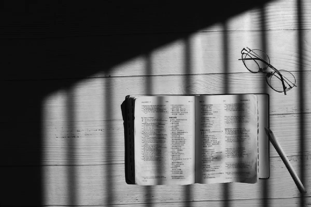 Open book with eyeglasses and pencil casting shadows in black and white.
