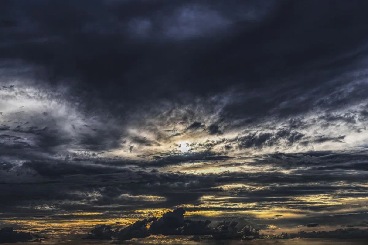 Moody dark clouds fill the sky as the sun sets, creating a dramatic atmosphere.