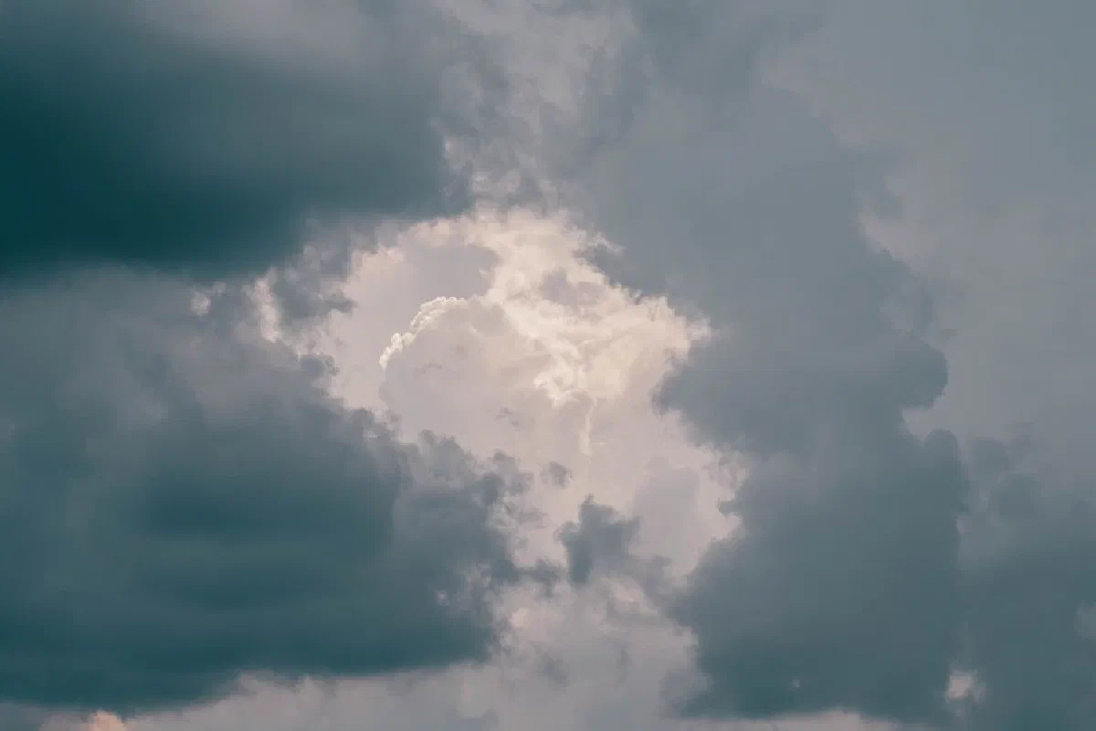 A powerful image of an overcast sky filled with dark, turbulent clouds and a peek of sunlight.