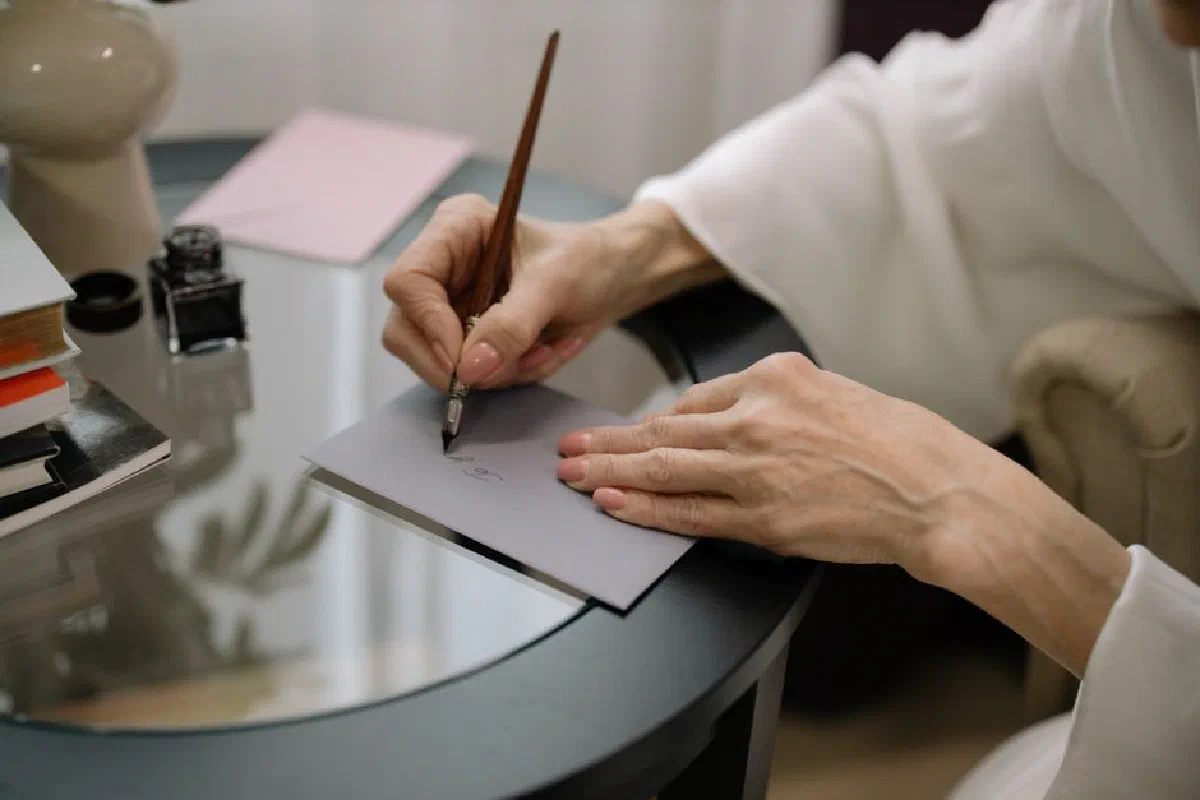 Close-up of hands elegantly writing on a gray envelope using a fountain pen.