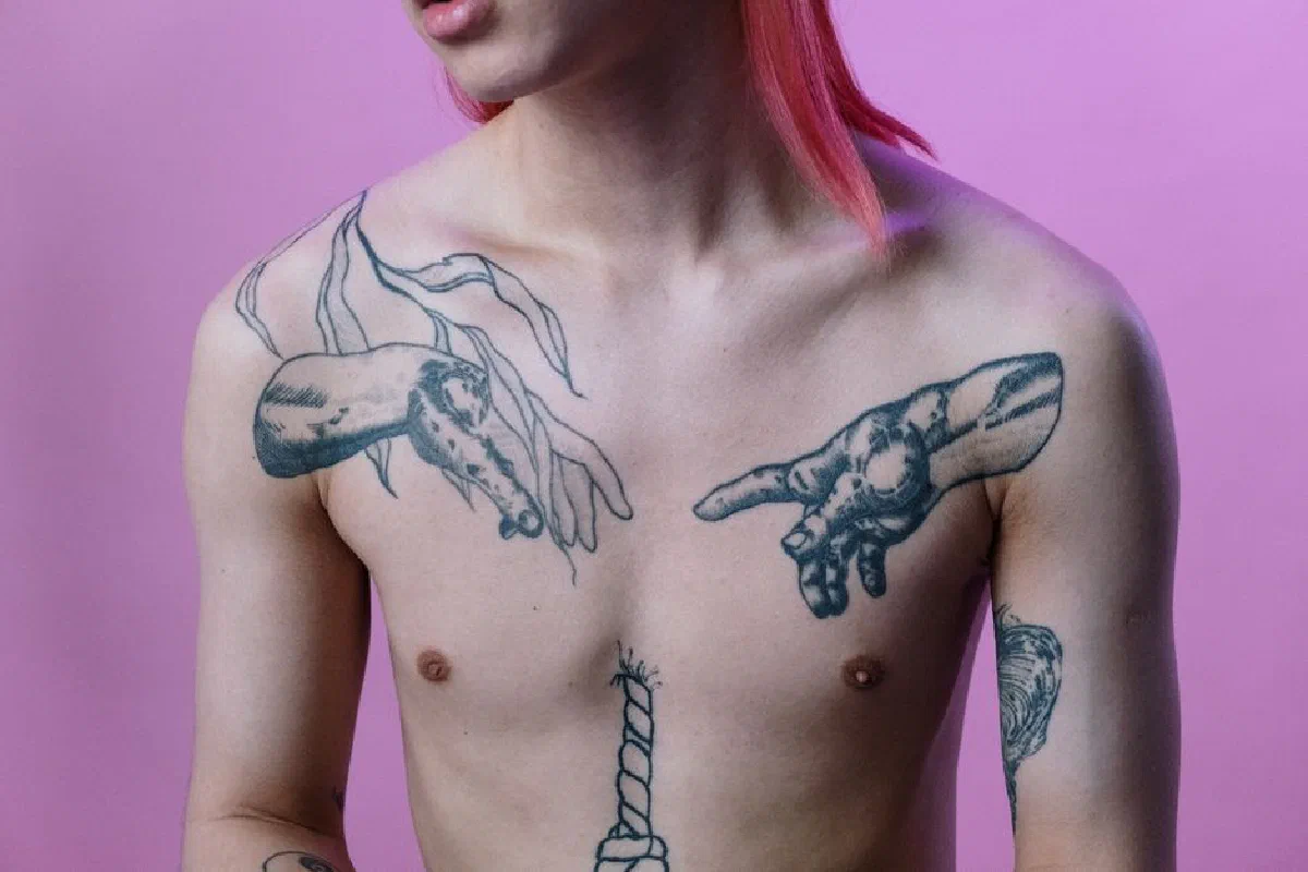 Artistic shot of a tattooed male torso with pink hair against a pink backdrop.