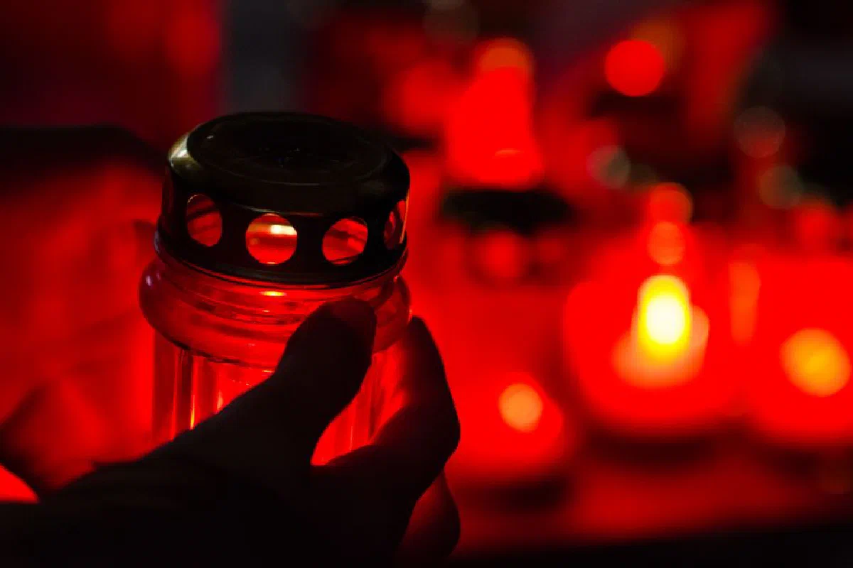 Silhouette of a hand holding a red candle during a nighttime remembrance ceremony.