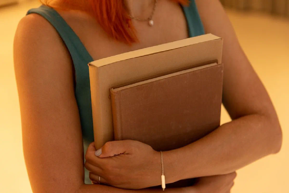 A woman in a blue dress holding books close to her chest in warm lighting.