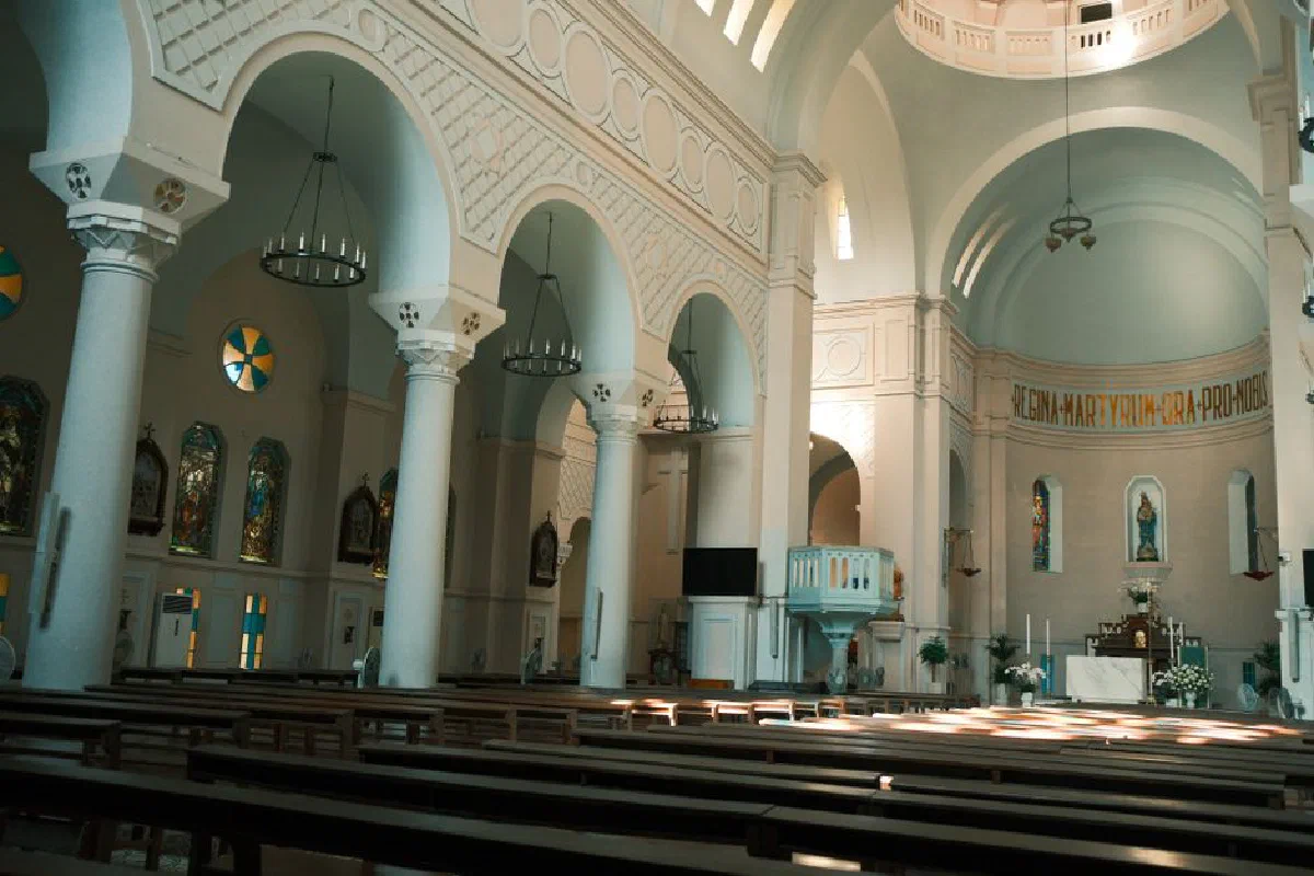 A stunning view of a catholic church interior with arches, stained glass windows, and empty pews, bathed in soft lighting.