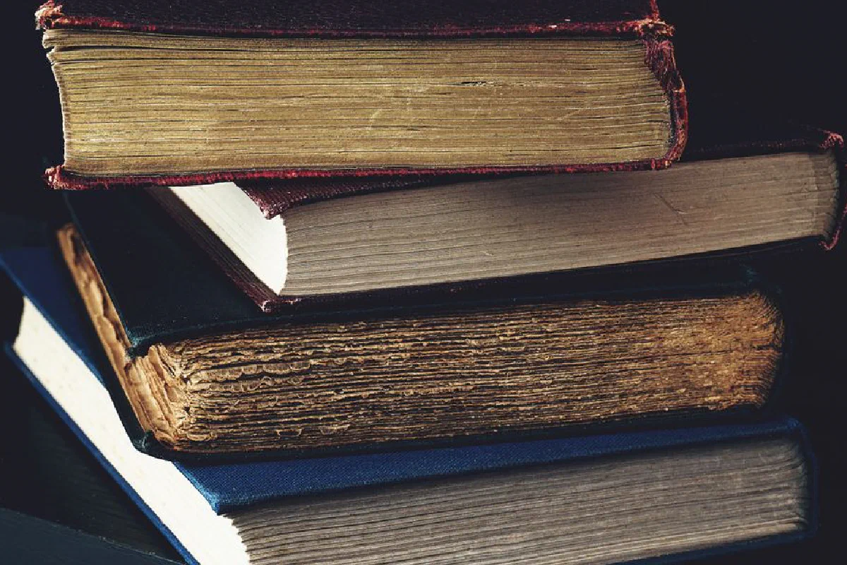 Close-up of a stack of vintage books with worn bindings, showcasing aged paper and textures.