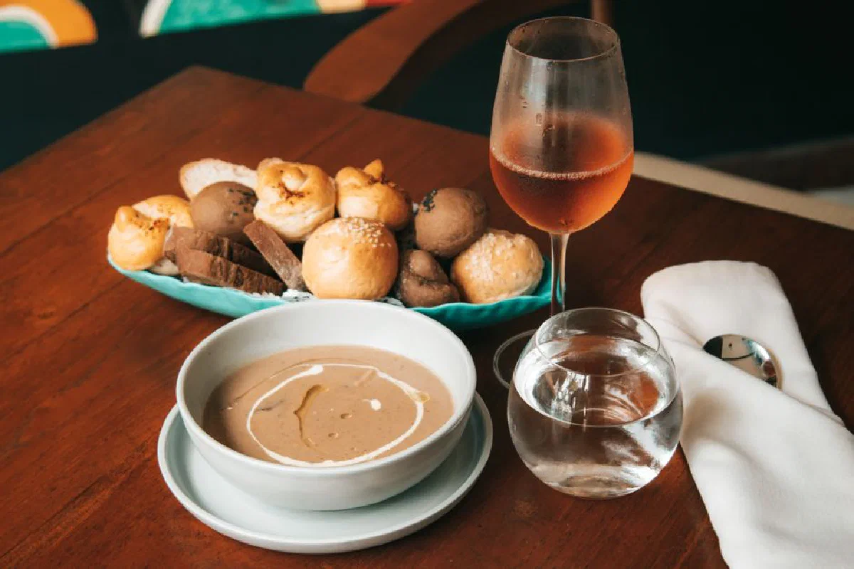 Warm meal setup featuring soup, assorted breads, a glass of wine, and a water glass on a wooden table.