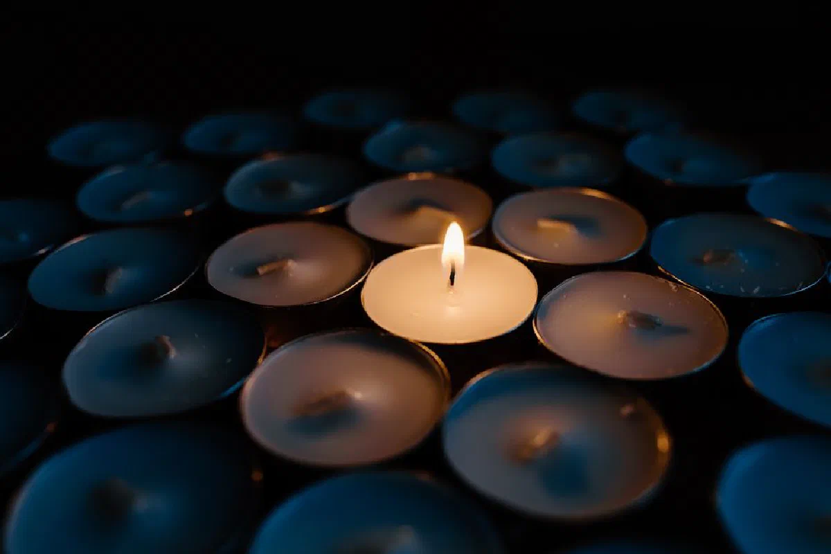 A single illuminated tealight candle amidst unlit ones, creating a warm glow in the dark.