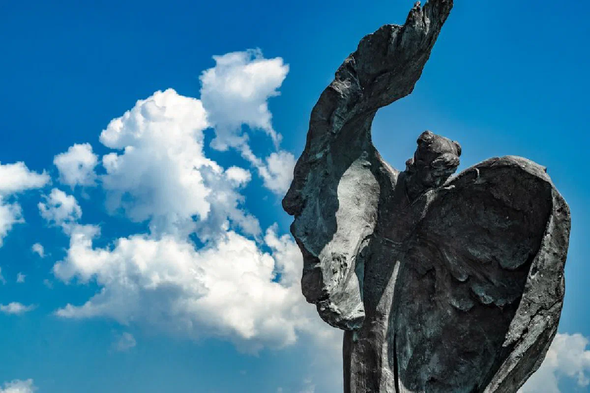 A stunning stone angel statue with wings, set against a vibrant blue sky with fluffy clouds.