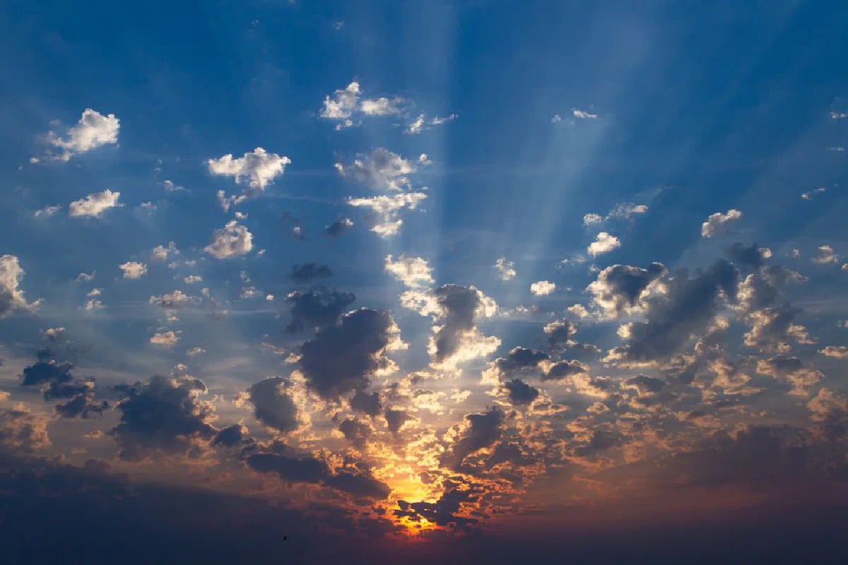 Stunning sunset with vibrant sunbeams and scattered clouds in a dramatic sky.