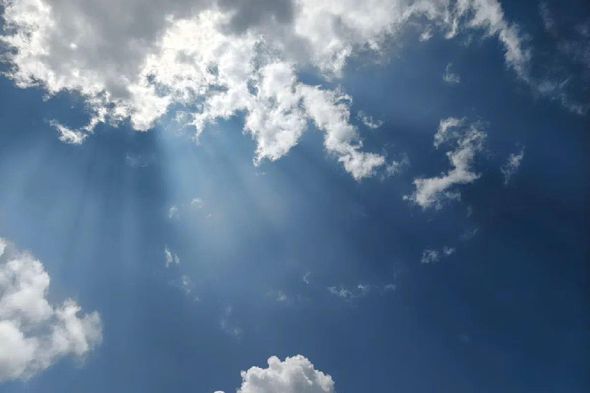 A tranquil view of fluffy clouds and sunbeams against a clear blue sky in Silchar, India.