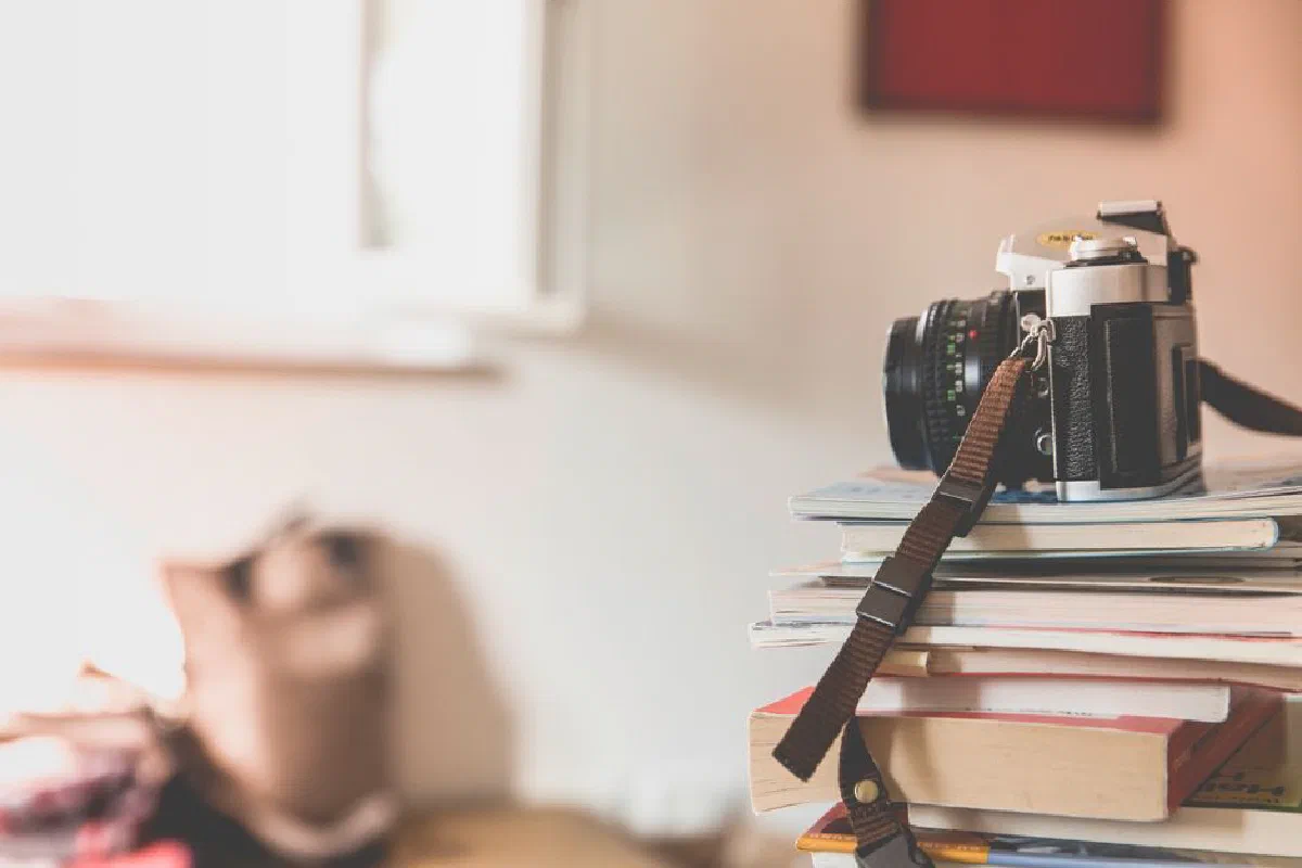 A vintage film camera rests on a pile of books in a well-lit, cozy indoor environment.