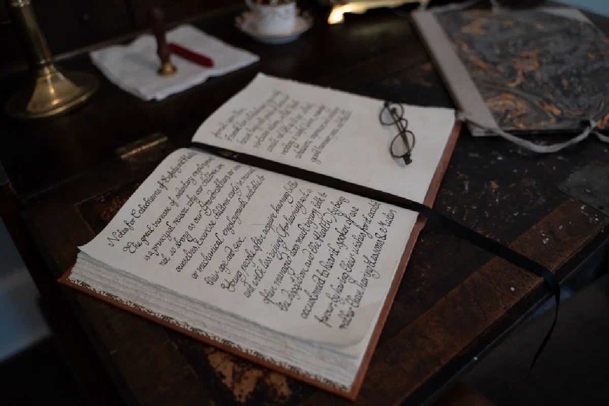 A vintage notebook with calligraphy text and eyeglasses on a wooden desk, creating a nostalgic scene.