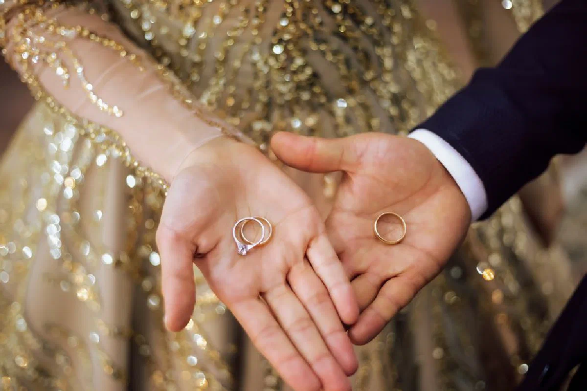 Close-up of bride and groom holding wedding rings, symbolizing unity and love.
