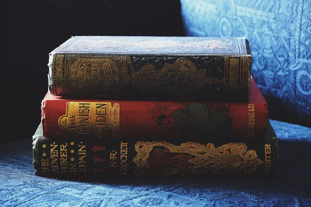 A stack of antique books with decorative bindings on a blue fabric sofa.