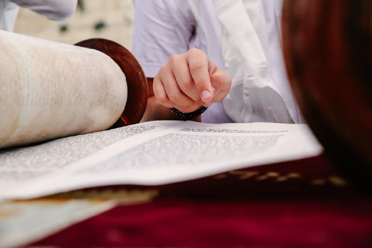 A hand pointing to text in a Torah scroll, symbolizing Jewish religious practices.
