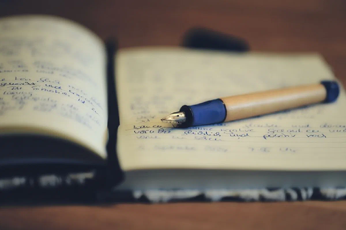 A close up of a fountain pen resting on an open notebook, highlighting handwriting and the writing process.