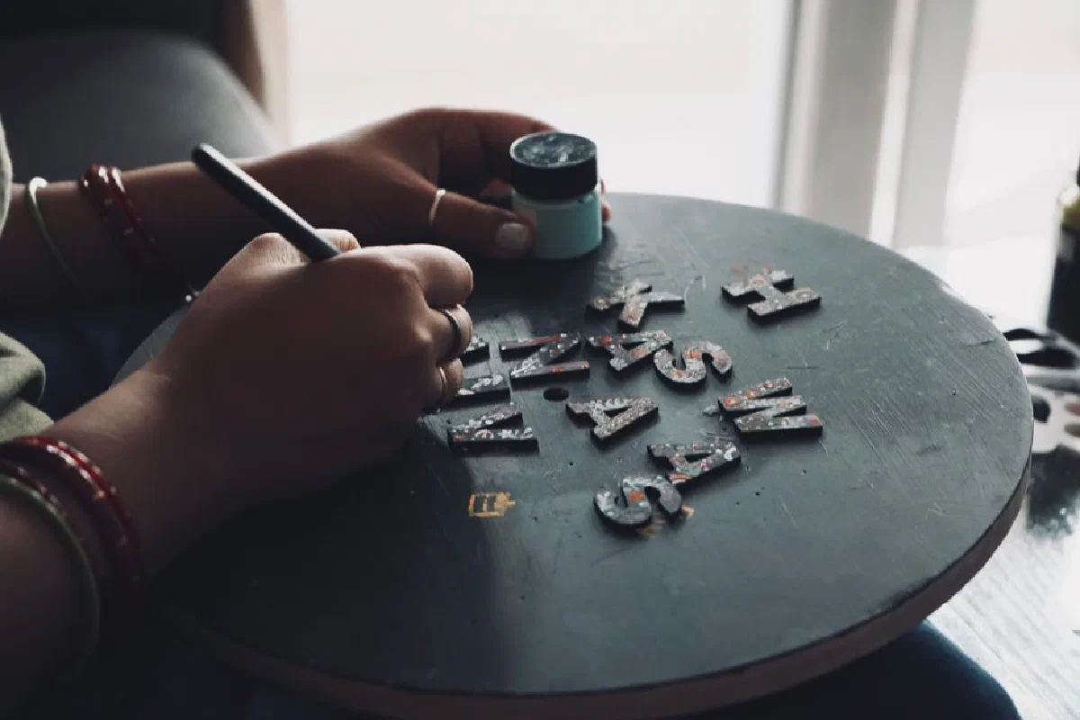 Hands painting letters on a circular board for crafting or design project.