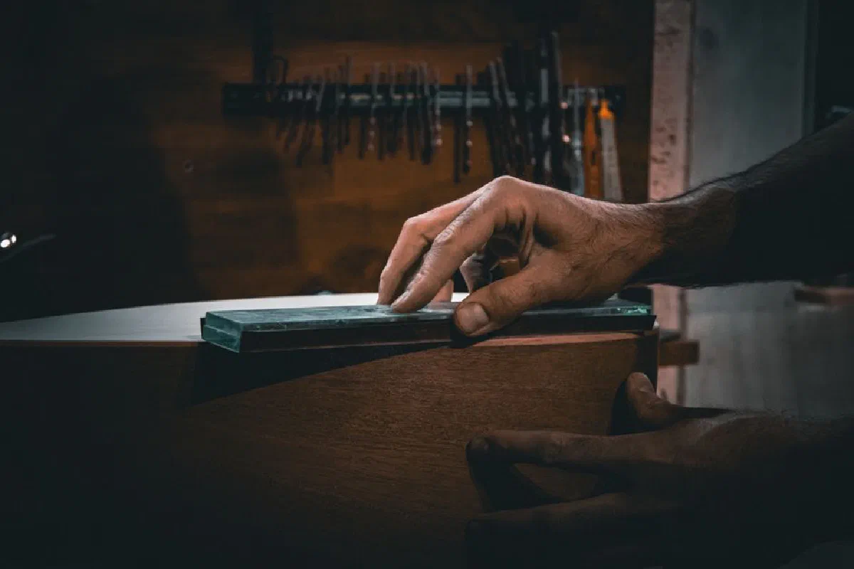 Detailed view of a craftsman sharpening a tool, highlighting skilled handwork in a workshop environment.