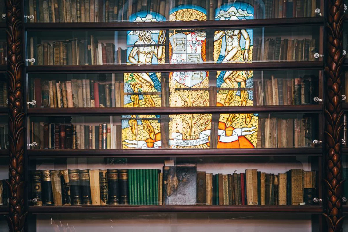 A vintage bookshelf with an ornate stained glass window reflecting vibrant colors.