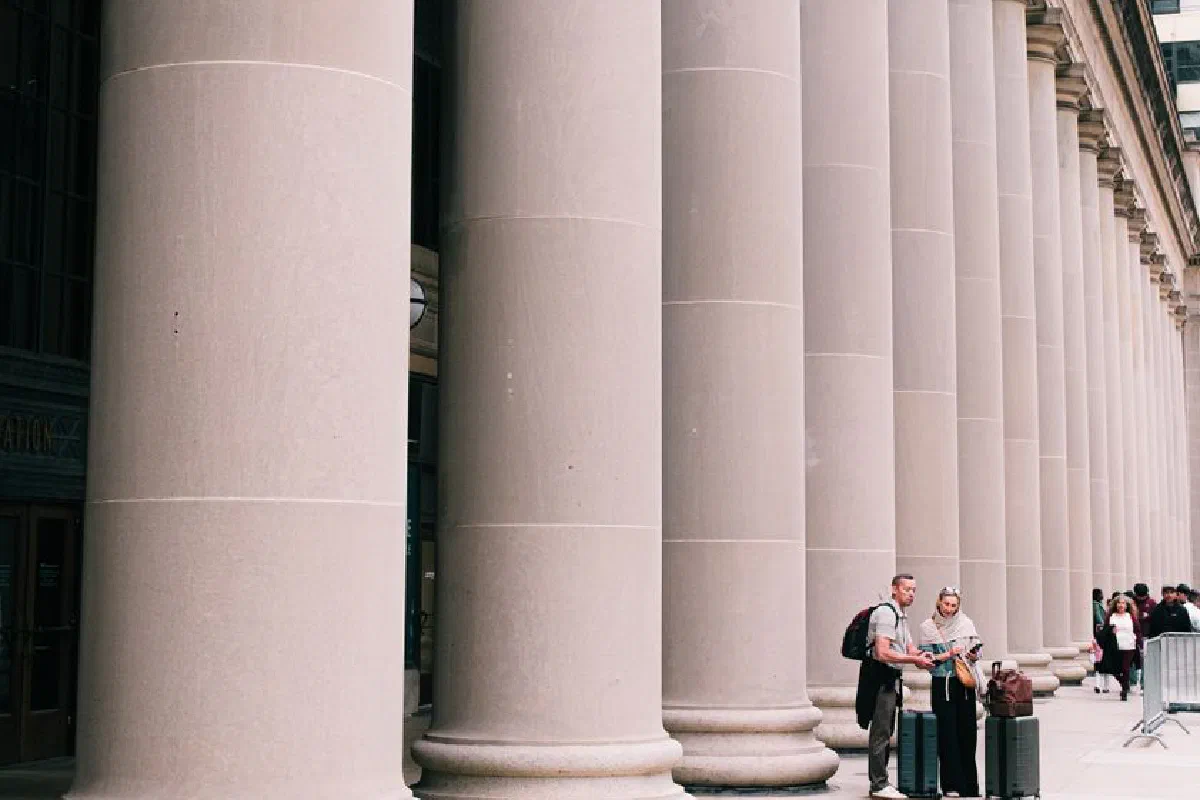 Two travelers stand beside large columns in Chicago, capturing the essence of urban exploration and architectural beauty.