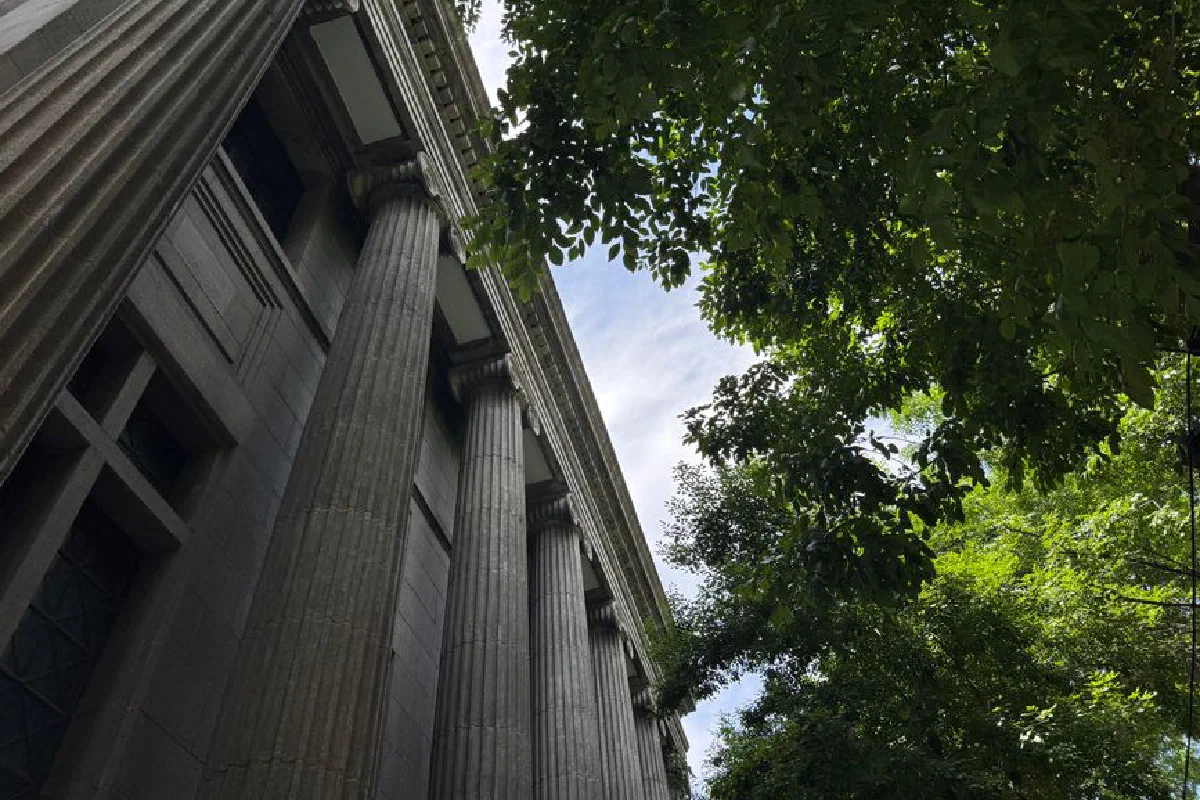 A low-angle view of a classical building with imposing columns and lush greenery against a clear sky.