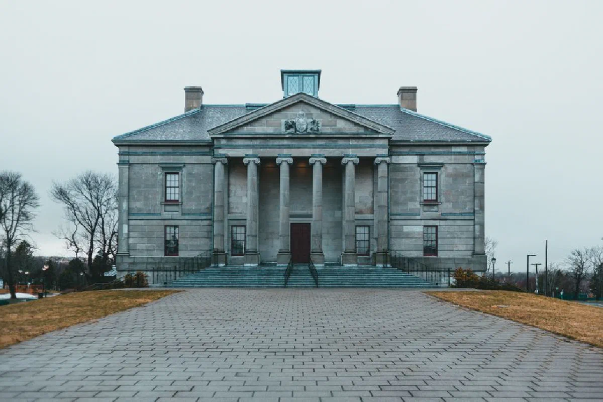 Exterior of aged stone building with columns and porch located near cobblestone pavement in gloomy weather
