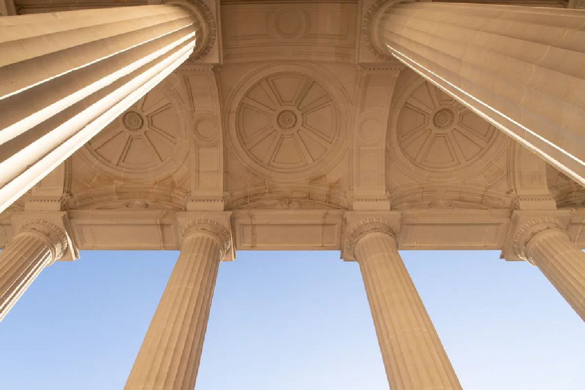 Low angle view of classical columns with ornate ceiling design under a clear blue sky.