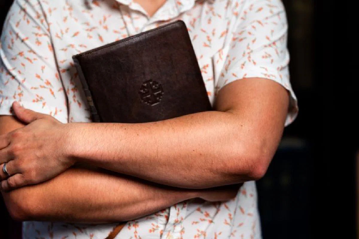 Close-up of a person holding a leather-bound book, suggesting themes of study and faith.