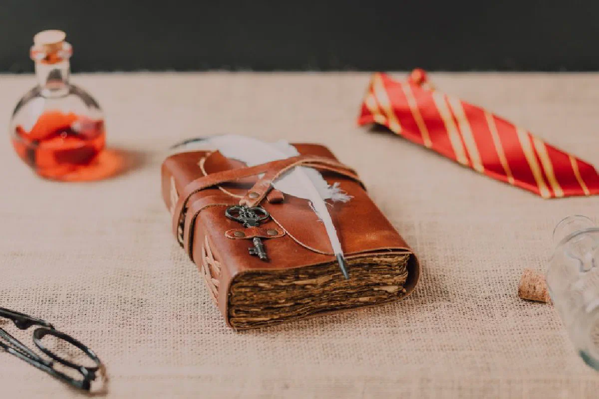 Leather-bound spell book with quill and potion bottle in a magical setting.