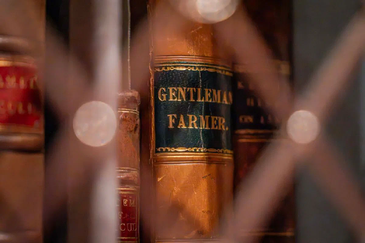 Close-up of vintage leather-bound books in a dimly lit library, featuring 'Gentleman Farmer' title.