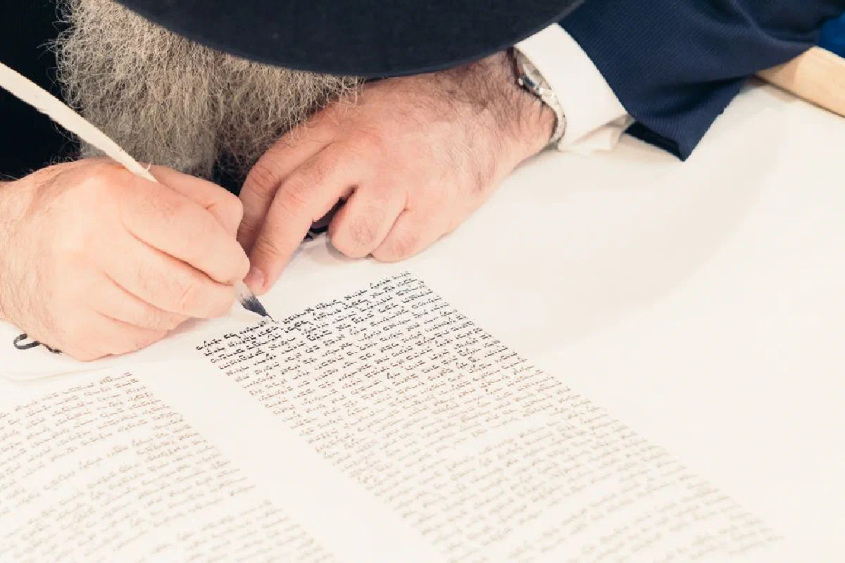Close-up of a man writing with a quill pen on a manuscript indoors, capturing the art of traditional handwriting.