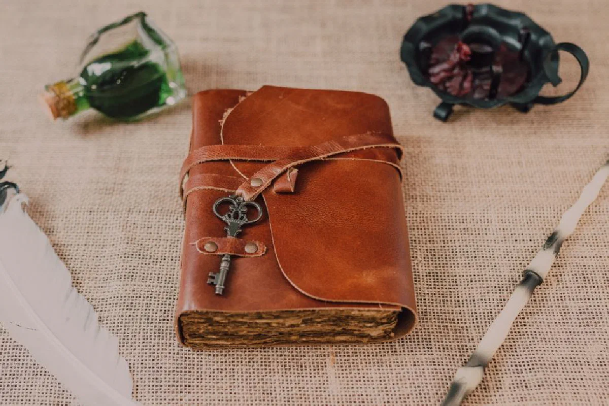 A vintage leather journal with an antique key, quill, and potion bottle on burlap fabric.