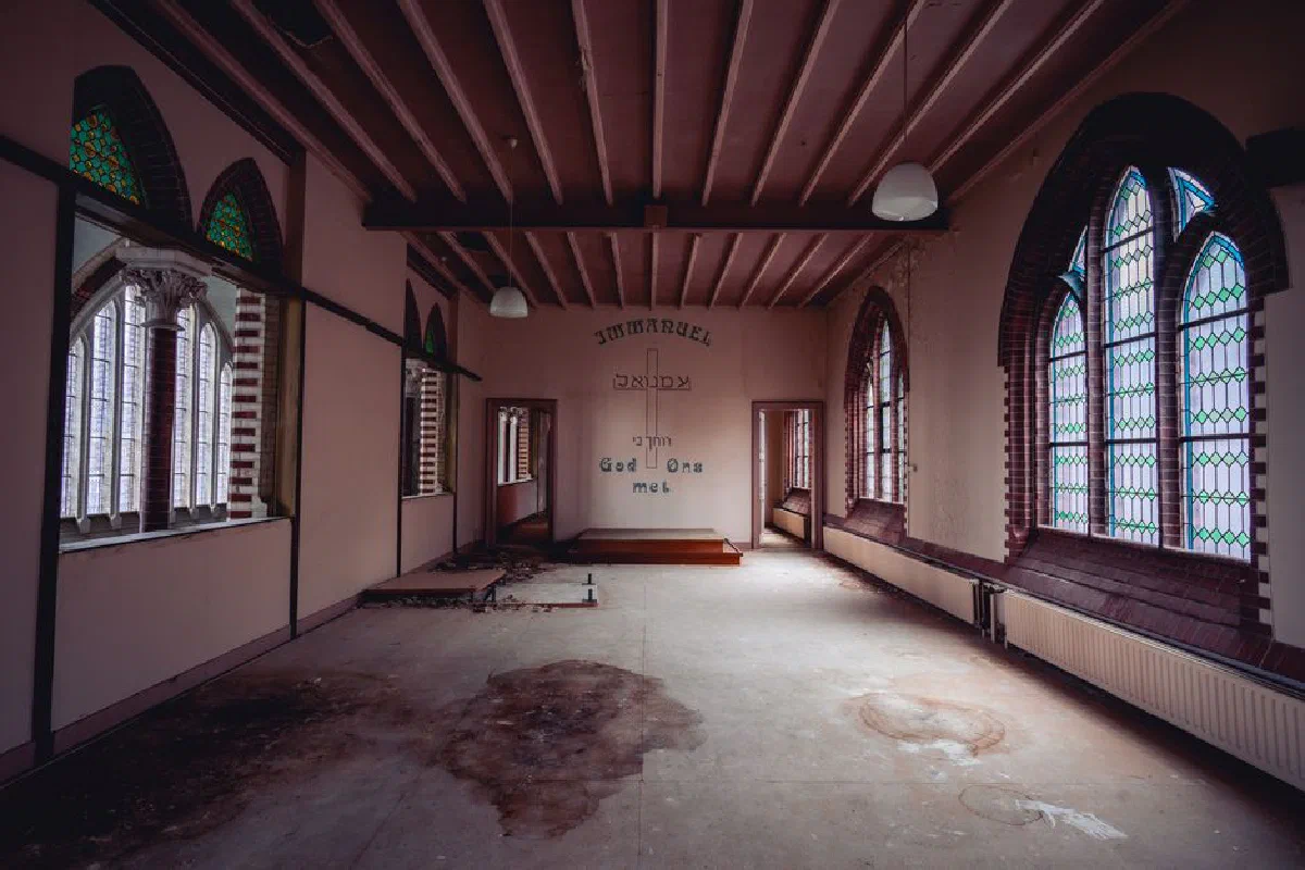 An empty, abandoned church interior featuring stained glass windows and religious inscriptions.
