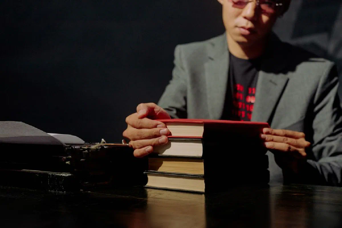 A businessman reading books by a typewriter in a dimly lit room.