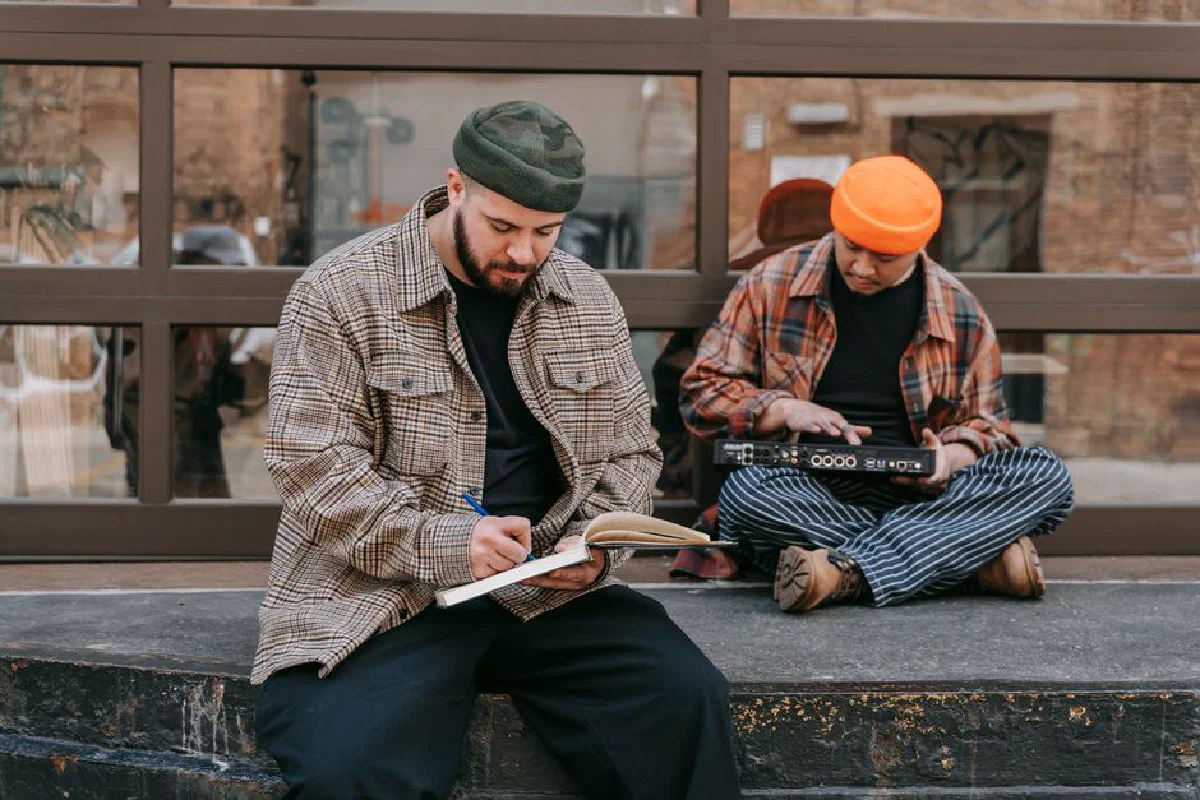 Two male musicians writing and creating music outside in a casual urban setting.