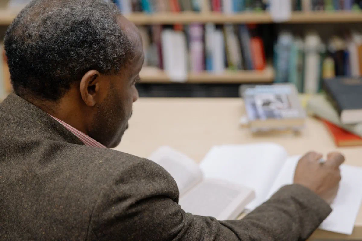 An adult African American man reading and writing in a library. Ideal for educational contexts.