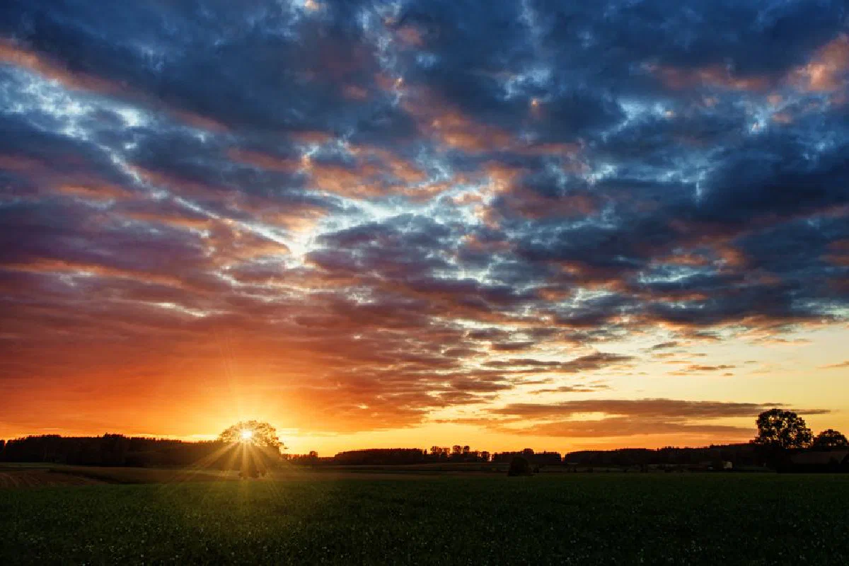 A vibrant sunset over a tranquil countryside field, showcasing a dramatic sky.