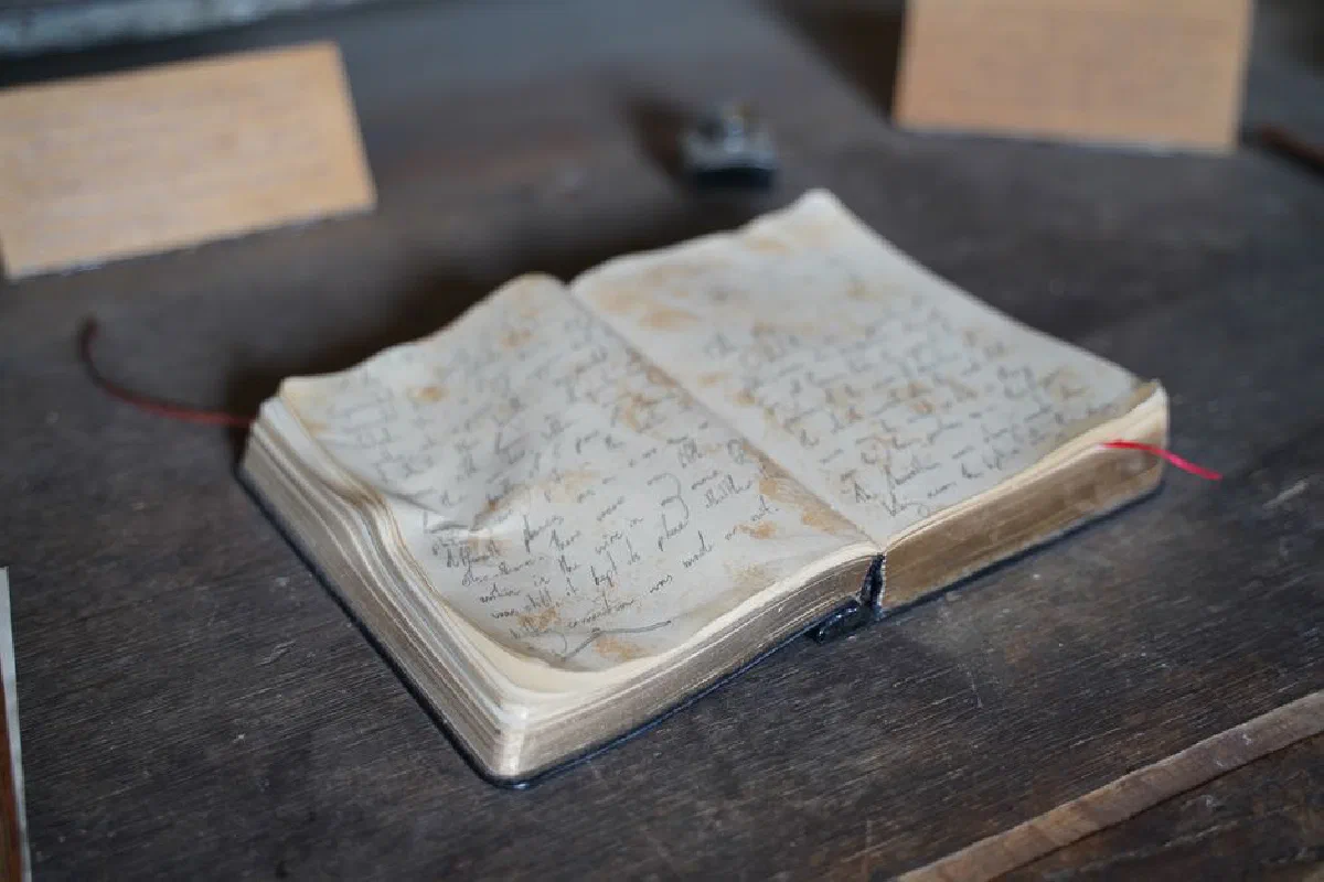 A close-up of an antique open book with handwritten pages on a rustic wooden table.