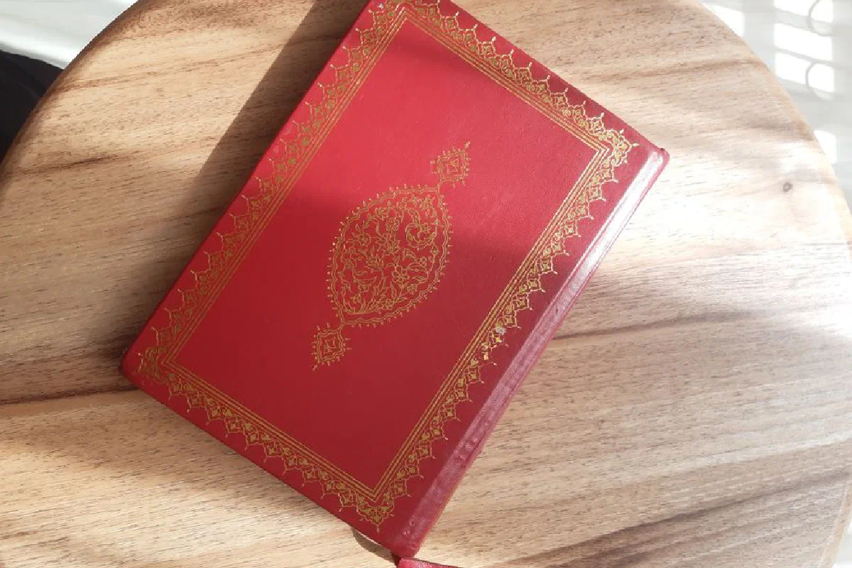 A beautifully decorated red leather book with golden details resting on a wooden table.