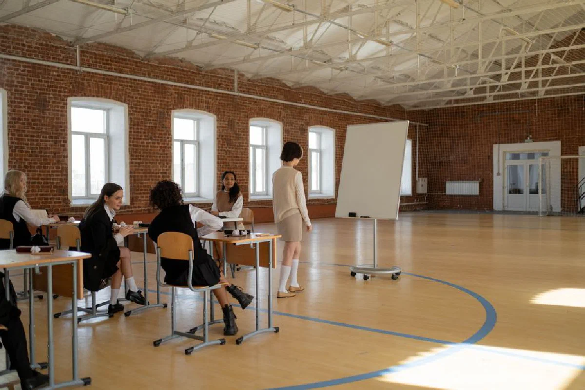 Students in school uniforms engaged in a lesson with a teacher in a spacious classroom.