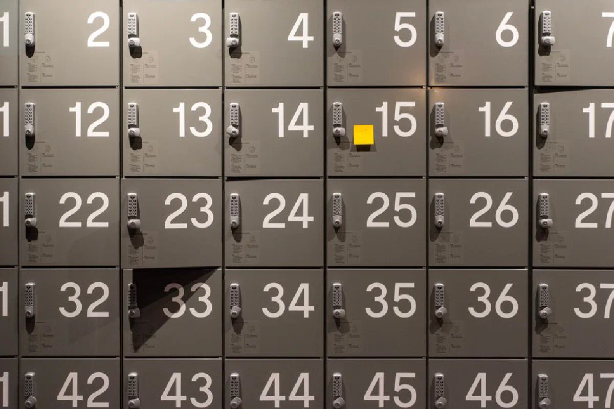 Gray lockers with electronic locks featuring numbers and a single yellow sticky note in the center.