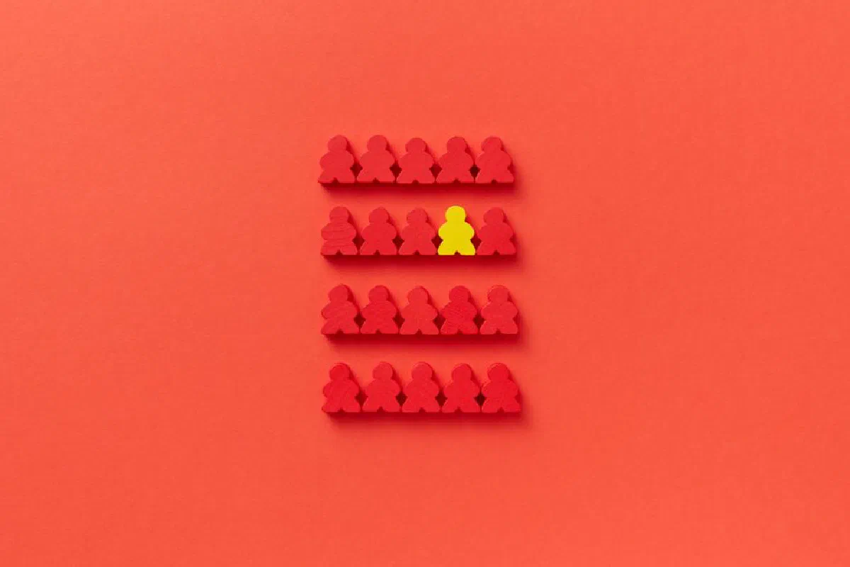 A standout yellow game piece among red pieces on a red background highlighting individuality.