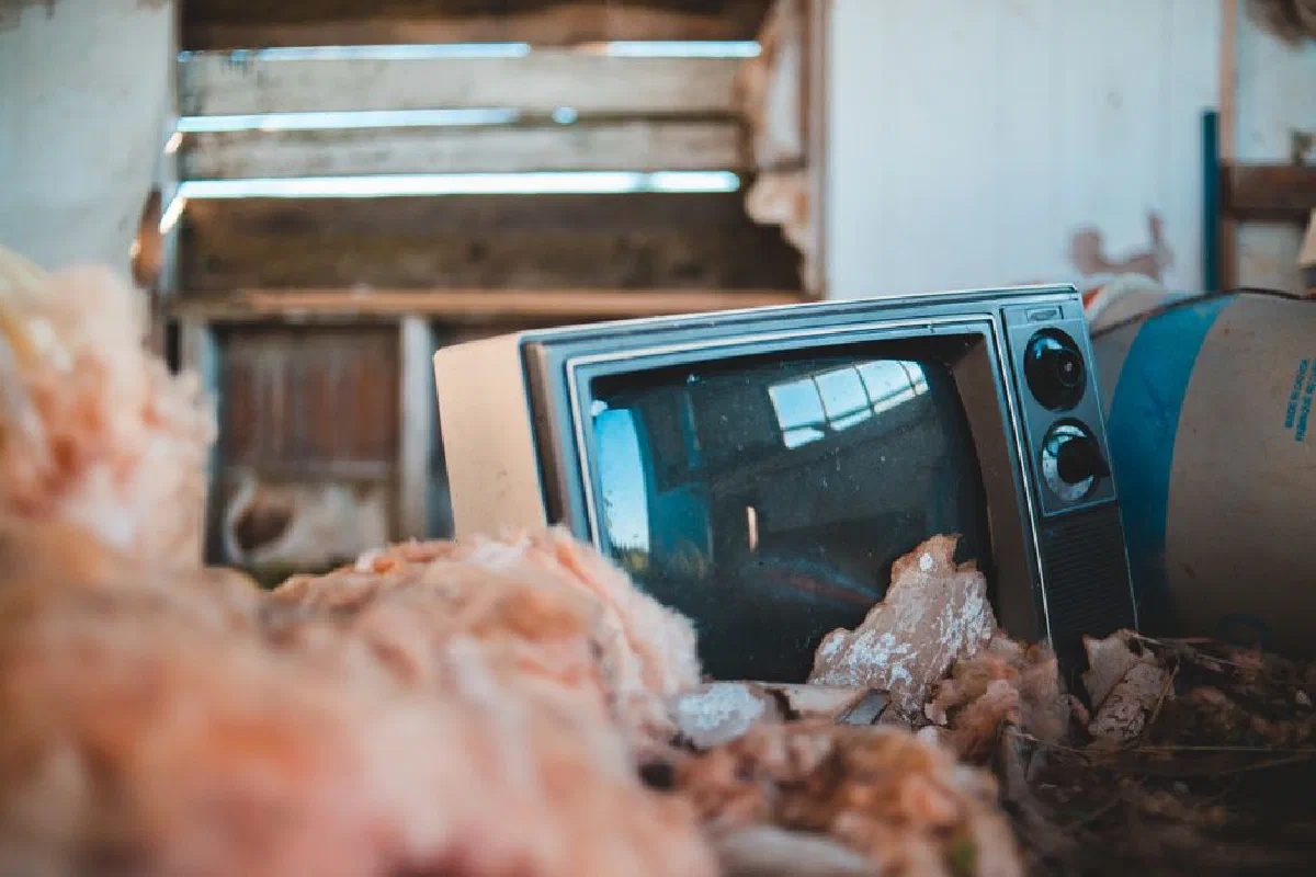 Ground level of retro television placed between various old objects in rural abandoned house in sunlight