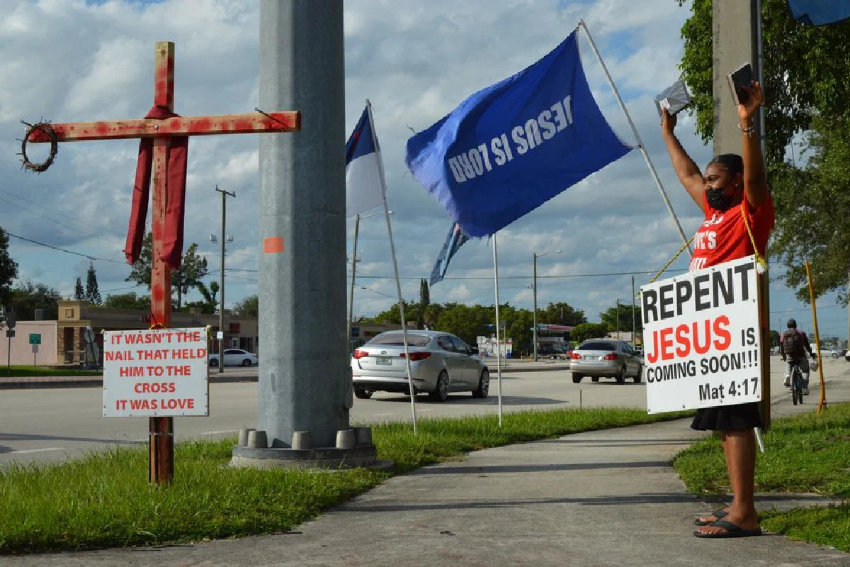Street scene depicting a person with a religious sign and cross advocating faith.