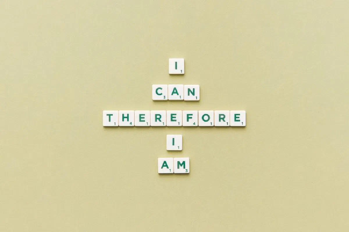 Inspirational phrase 'I Can Therefore I Am' arranged using Scrabble tiles on a green background.