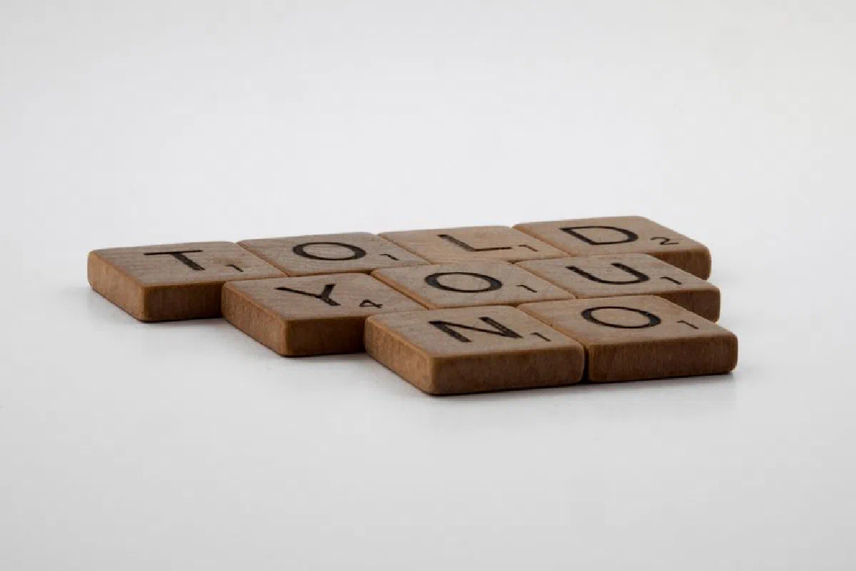 Scrabble tiles arranged to spell 'TOLD YOU NO', placed on a white surface.
