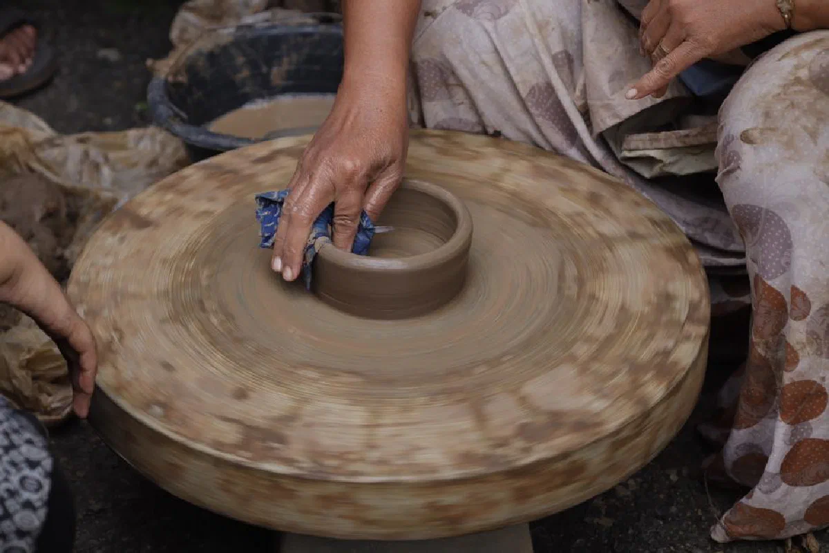Close-up of pottery being shaped by hand on a spinning wheel in a traditional setting.