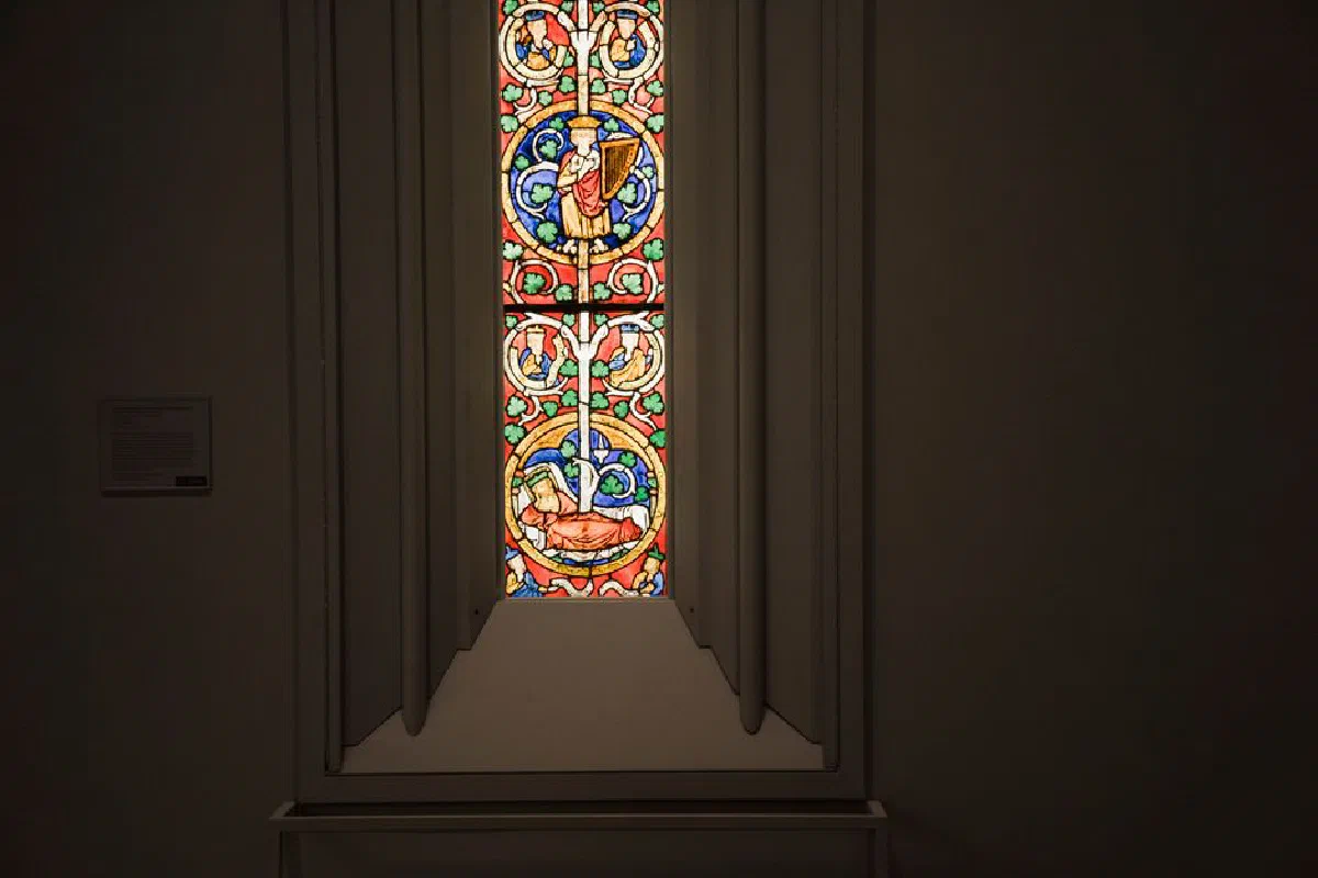 Narrow window with multicolored ornamental leaded glass in stucco frame located in dark grand cathedral
