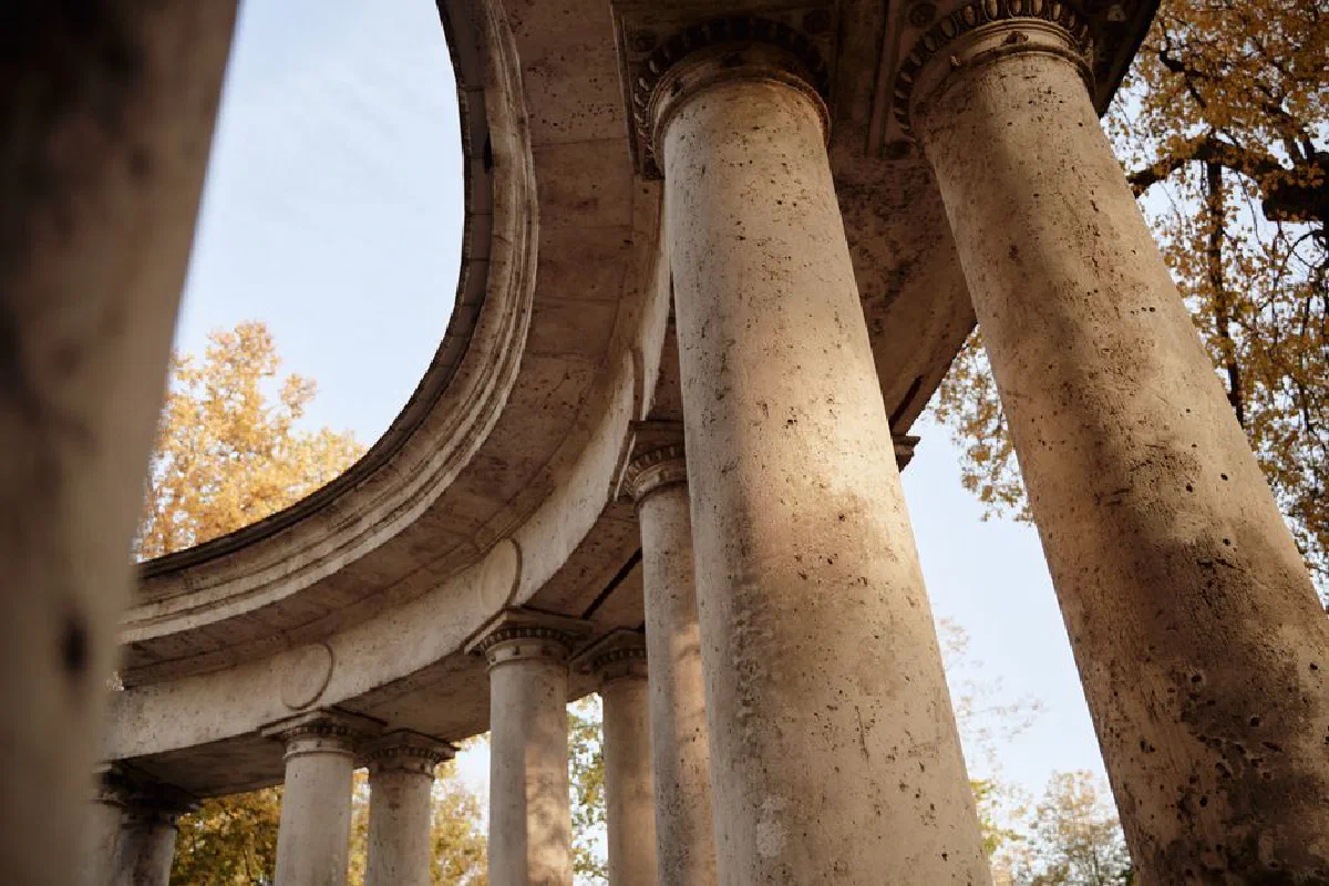 A photograph capturing a low-angle view of ancient stone columns and arches surrounded by autumn foliage.