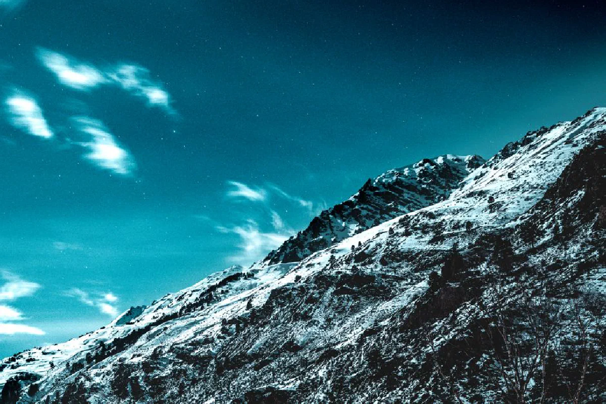 A breathtaking view of a snow-covered mountain at night, with a starry sky overhead.